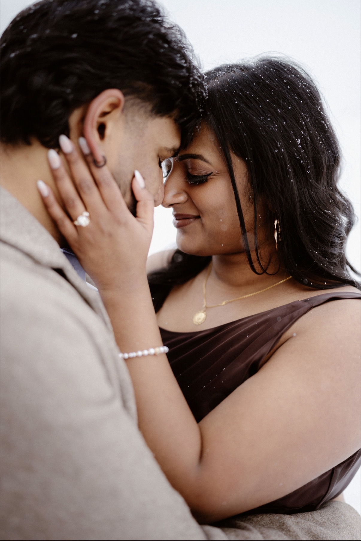 Close embrace in the snowfall, engagement ring catching the light